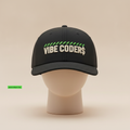 Vibe Coder$ hat in black, embroidered with VIBE CODER$ in cream under a green striped bar, on a mannequin head