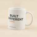 Built Different mug in white, printed with BUILT DIFFERENT in bold gray letters and quietly. in coral script