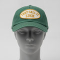 Est. Grind Varsity hat in green with a cream and gold THEY CALL IT LUCK patch, shown on a gray mannequin head